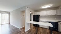 Located at 20800 Riverterrace Rd in South Chesterfield, Virginia, this single-floor residence offers a clean, modern aesthetic highlighted by dark hardwood-style flooring that runs consistently throughout the space. The open-concept layout connects the living area to the kitchen, creating a cohesive and functional flow. A sliding glass door in the living room fills the space with natural light and provides outdoor access, complemented by vertical blinds for privacy control.

The kitchen is well-appointed with white cabinetry, white countertops, and a full suite of black appliances, including a refrigerator, range, and dishwasher. A freestanding peninsula with a white surface and sleek black hairpin legs serves as both a prep area and casual dining spot, adding a contemporary touch to the kitchen's design.

The bedrooms are comfortably sized and feature individual closets with built-in shelving, neutral gray walls, and windows that allow natural light to brighten each room. A staircase with a black metal railing connects the main living level to additional areas. Throughout, the neutral color palette and consistent flooring create a unified, move-in-ready atmosphere.