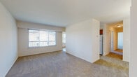 This single-floor residence offers a functional and well-organized layout designed to maximize comfort and usability. The open living area is generously sized, featuring neutral-toned wall-to-wall carpeting and crisp white walls that create a bright, clean atmosphere. A large picture window with a sliding glass panel floods the space with natural light and provides views of the surrounding exterior, including a balcony railing and neighboring greenery. A central dividing wall subtly separates the living area from the entry foyer, which features smooth hardwood-style flooring and a pendant light fixture overhead.

The galley-style kitchen runs along two parallel walls and is outfitted with warm oak cabinetry, dark laminate countertops, and a full suite of white appliances including a refrigerator, electric range, and dishwasher. Hardwood-style flooring continues throughout this space.

The bedrooms are carpeted and well-proportioned, each featuring windows with views of mature trees, offering a sense of privacy and connection to nature. The full bathroom includes a wood-toned vanity with a white countertop, tile flooring, and a tub-shower combination with tiled surround. A dedicated laundry area houses a full-size side-by-side washer and dryer beneath overhead storage cabinets, adding everyday convenience.
