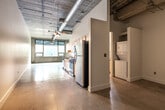 This single-floor loft showcases a striking industrial aesthetic throughout its well-planned layout. Polished concrete floors run seamlessly across the entire space, complementing the exposed concrete ceiling complete with visible ductwork, conduit, and track lighting — hallmarks of urban loft design. The open-plan living area is generously proportioned, bathed in natural light from large windows that frame views of surrounding greenery, and features a clean expanse of white walls that offer a versatile canvas.

The kitchen is thoughtfully designed with light maple cabinetry extending to the ceiling for ample storage, dark granite countertops, and a full suite of stainless steel appliances including a gas range, over-the-range microwave, and a full-size refrigerator. A stacked washer and dryer unit is conveniently located adjacent to the kitchen area, adding practical in-unit laundry access.

The bathroom features a full tub-shower combination accented by bold dark slate tile surround, a light wood vanity with a dark countertop, and concrete flooring that maintains the cohesive industrial feel. The overall ambiance of this loft is modern and urban, blending raw architectural elements with functional, contemporary finishes.