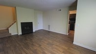 This two-floor residence offers a well-appointed interior designed for comfortable everyday living. The main living area makes a strong first impression with rich, dark hardwood flooring that runs throughout, providing warmth and a sense of continuity across the space. A sleek, dark-framed fireplace serves as a focal point on one wall, adding both character and a cozy ambiance to the room. The walls are finished in a soft, neutral tone that keeps the space feeling bright and open, complemented by a textured ceiling and clean white baseboards and trim. A dedicated HVAC vent along the wall ensures year-round climate comfort. The living area flows naturally toward the kitchen, which is visible through an open passage and features dark cabinetry and black appliances, creating a cohesive, modern aesthetic. A centrally located ceiling vent and multiple wall outlets reflect thoughtful utility placement throughout. The layout across two floors provides versatility and room to accommodate a variety of living arrangements, making this a functional and inviting home.