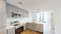 Located on the 11th floor at 801 N Orange St in Wilmington, Delaware, this modern one-bedroom unit offers a thoughtfully designed open layout with clean contemporary finishes throughout. Light hardwood flooring flows seamlessly across the entire space, complementing the bright white walls and creating a warm, cohesive aesthetic.

The open-concept kitchen and living area serves as the heart of the unit. The kitchen is outfitted with sleek grey flat-front cabinetry extending to the ceiling for generous storage, white quartz countertops, and a full suite of stainless steel appliances including a refrigerator, electric range, and over-the-range microwave. The adjacent living area benefits from an open, airy feel with clean sightlines throughout.

The bedroom is a well-proportioned retreat featuring dramatic floor-to-ceiling windows with black metal frames that frame sweeping elevated views of the Wilmington cityscape and surrounding neighborhoods. The room is bathed in natural light and includes a sliding-door closet for organized storage.

Throughout the unit, modern interior doors with matte black hardware, louvered closet doors, and recessed lighting add refined finishing touches. The overall ambiance is minimalist and contemporary, ideal for those seeking a sleek urban living experience in the heart of Wilmington.