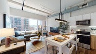 Located at 1 Martine Ave in White Plains, NY, this single-floor residence showcases a contemporary loft-inspired design that seamlessly blends industrial character with modern finishes. The open-concept living, dining, and kitchen area is anchored by soaring ceilings with exposed ductwork and structural beams, lending an urban, warehouse-style aesthetic. Large windows flood the living space with abundant natural light while framing views of the White Plains skyline.

The kitchen is thoughtfully appointed with two-tone cabinetry — sleek white upper cabinets paired with warm wood-finish lower cabinets — complemented by a marble-style tile backsplash, quartz countertops, and stainless steel appliances. A white high-top dining table with bar-style seating bridges the kitchen and living areas, enhanced by a striking geometric pendant light fixture overhead.

The living area offers generous space for relaxing and entertaining, with warm hardwood-style flooring running throughout. The bathroom features clean, minimalist design with large-format white wall tiles, mosaic floor tiles, and a walk-in shower enclosure. Throughout the residence, the interplay of natural textures, modern fixtures, and an open layout creates a bright, inviting atmosphere well-suited for urban living in Westchester County.