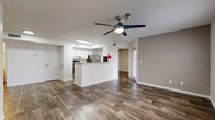 This single-floor unit is defined by a cohesive, open layout that connects the living area directly to the kitchen, creating a functional and visually spacious common area. Dark wood-look flooring runs consistently throughout, providing a warm contrast against the crisp white walls and baseboards. Ceiling fans are installed in the main living area and bedrooms, contributing to both comfort and airflow.

The kitchen is organized in a galley configuration and opens to the living space via a peninsula with light granite-style countertops. White shaker-style cabinetry lines both sides, complemented by a subway tile backsplash and stainless steel appliances, including a refrigerator, electric range, built-in microwave, and dishwasher. A stainless steel sink with a modern faucet is positioned beneath a window for natural light.

The bedrooms are well-proportioned, with one featuring a closet with bi-fold doors and elevated ceilings. Each room benefits from natural light, with windows fitted with horizontal blinds. The bathroom is finished with a granite-style vanity top, white cabinetry, a large mirror, and a full tub-shower combination enclosed by neutral large-format tile, maintaining a clean and consistent aesthetic throughout.