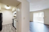 This single-floor unit offers a clean, functional layout designed for comfortable everyday living. The spacious living area is bathed in natural light from a large sliding glass door fitted with vertical blinds, which also provides direct access to the outdoors. Durable wood-look plank flooring runs throughout the living and hallway areas, lending a cohesive and modern aesthetic.

The galley-style kitchen is efficiently designed with white cabinetry lining both sides, granite-look countertops, and black appliances including a refrigerator, electric range, and built-in range hood. A hallway connects the main living space to the private areas of the unit, including two carpeted bedrooms. Both bedrooms feature windows with blinds that allow for natural light and outdoor views. The primary bedroom includes a ceiling fan for added comfort.

The bathroom is neatly appointed with a white vanity, granite-look countertop, a large mirror with a lighted fixture above, and wood-look flooring that ties the space together. The unit's neutral color palette of warm whites and beige tones throughout creates a bright, inviting atmosphere. A dedicated hallway enhances the flow and privacy between living and sleeping areas, making this a practical and welcoming space.