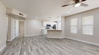 This single-floor home presents a clean, modern aesthetic with a neutral color palette and consistent design choices throughout. The open-concept living and dining area flows seamlessly into the kitchen, unified by light gray wood-look flooring and a textured ceiling. Ceiling fans are installed throughout the main living spaces and bedrooms, contributing to both comfort and style. Natural light enters through multiple windows fitted with white plantation blinds.

The kitchen is well-appointed with white shaker-style cabinetry, stainless steel appliances including a range, microwave, refrigerator, and dishwasher, along with light-toned countertops. A peninsula with pendant lighting above serves as a natural divider between the kitchen and living area, adding both function and visual interest.

The bedrooms feature plush carpeting and ceiling fans, with at least one room offering access to a spacious walk-in closet with shelving. The primary bathroom includes a dual-sink white vanity with brushed gold hardware, a large mirror, and tile-look flooring that complements the rest of the home. An additional flexible room with wood-look flooring provides versatile use as an office or bonus space. Overall, the home conveys a bright, well-maintained, and move-in-ready atmosphere.