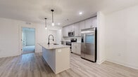 Located at 9121 Pine Forest Road in Pensacola, Florida, this well-appointed single-story home offers four bedrooms, two bathrooms, and a thoughtfully designed layout across a generously sized floor plan. The open-concept kitchen and living area serves as the heart of the home, showcasing a large center island with granite countertops, an undermount sink with a matte black faucet, and pendant lighting overhead. White shaker-style cabinetry reaches toward the ceiling, complemented by a full suite of stainless steel appliances including a refrigerator with ice maker, electric range, and over-the-range microwave. Light wood-look luxury vinyl plank flooring flows throughout the main living areas, adding warmth and continuity. The spacious primary bedroom features plush carpeting, a ceiling fan, and direct access to a private en-suite bathroom equipped with a granite-topped vanity and a walk-in glass-enclosed shower. Additional bedrooms are carpeted and include ceiling fans and natural light from well-placed windows. Multiple walk-in closets with wire shelving systems provide ample storage. The secondary bathroom mirrors the refined finishes found throughout. A dedicated utility room adds further practicality to this clean, modern home.