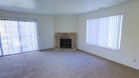 This two-floor residence offers a comfortable and functional layout designed to suit a variety of lifestyles. The main living area immediately draws attention with its corner brick fireplace, which serves as a warm and classic focal point in the room. The raised stone hearth adds a traditional charm that complements the neutral color palette throughout the space. Plush wall-to-wall carpeting provides a soft, inviting feel underfoot, while the light-toned walls keep the atmosphere bright and open. Natural light flows generously into the living area through large windows dressed with vertical blinds, offering both privacy and light control. A sliding glass door further enhances the connection to the outdoors, suggesting access to a patio or exterior area. The clean, minimalist interior provides a versatile canvas that can be adapted to a wide range of décor styles. Spanning two floors, the home offers ample space for both living and private quarters, making it well-suited for individuals, couples, or families seeking a straightforward, well-appointed residence with classic architectural details and practical amenities throughout.