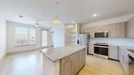 This 2-bedroom, 2-bathroom residence delivers a clean, modern aesthetic across a single, efficiently organized floor. The kitchen serves as a standout feature, showcasing light wood-grain cabinetry, granite countertops, a subway tile backsplash, and stainless steel appliances including a refrigerator with ice maker, range, microwave, and dishwasher. A large center island with additional granite surface space provides ample room for meal preparation and casual dining. Light hardwood-style flooring runs throughout the kitchen and bathrooms, contributing to a bright, cohesive feel.

The primary bedroom is generously sized, featuring plush wall-to-wall carpeting, a ceiling fan, and direct access to a private en-suite bathroom. The primary bath is equipped with a dual-sink vanity topped with granite counters, a backlit mirror, and a walk-in closet with double hanging rods. A glass-enclosed shower completes the suite. The second bedroom also offers soft carpeting, a ceiling fan, and a window with exterior views, providing ample natural light. A second full bathroom serves this bedroom and guests. Both bedrooms are bright and neutral, offering a versatile canvas. Two hallways and additional closets enhance the practical storage options throughout this well-designed residence.