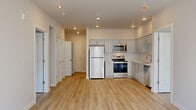 Located at 1938 NW 25th Ave in Portland, Oregon, this single-floor unit offers a clean, contemporary design defined by a consistent palette of white walls, white trim, and light wood-tone luxury vinyl plank flooring throughout. The open-concept layout connects the living area and kitchen, creating a functional and airy feel.

The kitchen is well-appointed with gray shaker-style cabinetry, white countertops, a stainless steel refrigerator, electric range, microwave, and dishwasher, all illuminated by recessed lighting overhead. Ample cabinet storage lines the walls, providing generous workspace and organization.

The living area benefits from multiple windows fitted with horizontal blinds, allowing natural light to fill the space. A door provides additional access from the living area. The bedroom features its own windows with natural light and connects directly to a spacious walk-in closet equipped with wire shelving and hanging rods for organized storage.

The bathroom includes a wide vanity with white quartz-style countertops, gray cabinetry with brushed nickel hardware, and a large mirror with integrated lighting. Light wood-tone flooring continues here, maintaining a cohesive aesthetic throughout the unit. The overall ambiance is bright, neutral, and move-in ready.