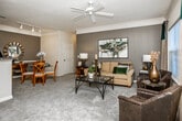 Located at 2416 Columns Dr in Cumming, Georgia, this single-floor residence offers a well-designed layout with a variety of distinct living spaces. The entryway opens into a carpeted living room adorned with elegant crown molding and a ceiling fan, creating a welcoming first impression. A decorative console table and accent wall art set the tone for the thoughtfully styled interior throughout.

The living room features large windows that invite natural light and provide outdoor views, complemented by a bold gray accent wall and crown molding details. The adjacent dining area continues the refined aesthetic with a two-tone gray wall treatment, chair rail molding, and a glass-top dining table.

The galley-style kitchen is lined with warm honey-toned wood cabinetry, dark countertops, and hardwood-style flooring, providing ample storage and workspace. White appliances including a refrigerator, range, microwave, and dishwasher complete the functional setup.

The residence includes multiple bedrooms, each carpeted and featuring large windows with natural light. One bedroom stands out with a rich emerald green accent wall, while another offers a neutral, warm palette. Both bathrooms include white vanity cabinetry with dark countertops, hardwood-style flooring, and shower-tub combinations, offering clean and practical finishes throughout.