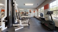 The B Fit Fitness Center at 1100 Townsend Blvd in Fredericksburg, Virginia, is a thoughtfully designed, single-floor exercise facility that provides a comprehensive workout environment. The space is defined by its bold aesthetic, featuring a striking orange accent stripe that runs along the upper portion of the walls, contrasting against a clean white backdrop — creating an energetic and motivating atmosphere throughout.

The fitness floor is finished with durable dark rubber tile flooring, ideal for both cardio and strength training activities. A full-wall mirror is positioned along one side of the room, enhancing the sense of openness while allowing members to monitor their form. The space is well-lit by overhead fluorescent lighting and benefits from generous natural light streaming through large windows, which also offer pleasant views of the surrounding tree-lined outdoor scenery.

Equipment on the floor includes a multi-station cable and weight machine, an adjustable bench press, elliptical trainers, a stair climber, a recumbent bike, and a rowing machine, offering a well-rounded selection for members at varying fitness levels. A flat-screen television is mounted on the wall for entertainment during workouts.

Near the entrance, a white wall-mounted shelf with coat hooks provides convenient storage, and a glassed interior partition adds a refined architectural touch. The layout is open and spacious, allowing for comfortable movement between stations.