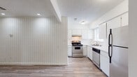 This single-floor residence offers a clean, functional layout with a cohesive design throughout. The kitchen is a standout feature, finished with crisp white cabinetry extending to the ceiling, stainless steel appliances including a gas range, dishwasher, and refrigerator, and a double stainless steel sink positioned beneath a window that allows natural light to fill the space. Light wood-look flooring runs continuously through the kitchen and into the adjoining living and dining areas, creating a seamless and unified aesthetic.

The main living area is distinguished by a bold vertical shiplap accent wall painted white, adding texture and architectural character to the open space. Recessed lighting and a textured ceiling complement the room's clean lines. A wide entryway connects the living area to the rest of the unit, maintaining an open and airy feel throughout.

The bathroom features an extended white vanity countertop with a single sink, dual black-framed mirrors, and wall-mounted sconce lighting for a modern touch. Wood-look flooring continues here as well, and an adjacent doorway provides direct access to a walk-in closet, adding practical storage to the space. Overall, the residence presents a well-maintained, move-in ready interior with consistent finishes and a bright, neutral palette throughout.
