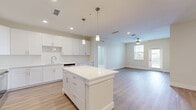 Located at 1023 Gull Ln in Melbourne, FL, this well-appointed 4-bedroom, 2-bathroom single-story home offers a clean, modern aesthetic throughout. The open-concept living area seamlessly connects the kitchen, dining, and living spaces, creating an expansive and airy atmosphere. The kitchen is a standout feature, boasting crisp white shaker cabinetry, a large center island with white quartz countertops, pendant lighting, and a full suite of stainless steel appliances including a refrigerator, range, microwave, and dishwasher. Light wood-tone flooring flows through the main living areas, complementing the neutral color palette. The living room benefits from natural light streaming through windows fitted with blinds and includes a ceiling fan for added comfort. Each bedroom features plush carpeting, ample closet space with wire shelving systems, and access to natural light. The primary bedroom connects directly to a sleek en-suite bathroom complete with a dual-sink floating vanity, an illuminated mirror, and a glass-enclosed tiled shower. A dedicated laundry area and additional bathroom add convenience. The private balcony offers a pleasant outdoor retreat with views of the surrounding landscaped greenery and neighborhood streetscape.