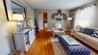 Located at 38 Stenton Ct in Trenton, NJ, this single-floor, one-bedroom, one-bathroom home offers a thoughtfully organized layout across a compact yet functional footprint. Warm hardwood flooring runs throughout the living areas and bedroom, creating visual continuity and a welcoming ambiance.

The living room is a comfortable, well-lit space featuring neutral gray walls, decorative rustic wall-mounted shelving, and natural light from a window fitted with sheer curtains. A ceiling-mounted wall unit provides climate control. The space flows naturally toward a hallway leading to the remaining rooms.

The kitchen features warm wood cabinetry, tile flooring, subway tile backsplash, and a gas range with overhead microwave. A window above the counter brings in natural light and overlooks greenery outside. Adjacent to the kitchen, the dining area accommodates a round table with seating for four, set against light-toned walls.

The bedroom comfortably fits a full-sized bed alongside a dresser and features hardwood floors, natural light from a window, a ceiling fan, and a closet. The bathroom includes a full-sized soaking tub with a tiled surround and shower curtain. A connecting hallway ties all rooms together efficiently.