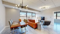 Located in the heart of downtown Charleston, West Virginia, this single-floor unit at 901 Lee St presents a thoughtfully designed contemporary interior with high-end finishes and urban views. The open-concept living and dining area is anchored by bold orange leather seating, a glass coffee table, and sputnik-style chandeliers that add a mid-century modern flair. Large windows throughout frame expansive city and mountain views, flooding the space with natural light.

The kitchen is a standout feature, showcasing floor-to-ceiling dark wood cabinetry, a dramatic stone-veined backsplash, a generous waterfall-edge marble island with bar seating, and a full suite of stainless steel appliances including a range, dishwasher, and French door refrigerator. A tray ceiling detail with recessed lighting enhances the kitchen's refined character.

The bedrooms are calm and well-appointed, with one featuring large windows overlooking the cityscape. Bathrooms reflect the same modern sensibility, with floating vanities, white quartz countertops, gray tile, and a glass-enclosed walk-in shower. Additional built-in shelving provides practical storage throughout.