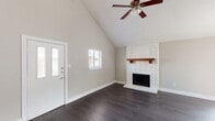 This single-story home offers a thoughtfully designed layout with a variety of finishes and architectural details that create a welcoming and functional living environment. The living area immediately impresses with its dramatic vaulted ceilings that rise sharply upward, amplifying the sense of space and openness. A striking white-painted brick fireplace with a warm wood mantel serves as the room's focal point, while dark hardwood flooring runs throughout and a ceiling fan provides year-round comfort. Natural light filters in through windows fitted with blinds, and the front entry door features a sidelight panel that adds to the bright, airy atmosphere. The kitchen is designed for efficiency, featuring a classic galley-style layout with white cabinetry, granite countertops, white subway tile backsplash, black appliances including a refrigerator, microwave, and range, and track lighting overhead. The bedroom areas offer plush carpeting underfoot and neutral wall tones, with one bedroom showcasing a large sliding glass door fitted with vertical blinds that allows abundant natural light. Ceiling fans are present throughout, and textured ceilings add subtle character to the more private areas of the home. Overall, the space balances modern updates with comfortable, classic design elements.