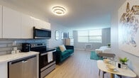 Located at 14040 Biscayne Blvd in North Miami, FL, this thoughtfully designed studio offers a bright, open-plan layout that seamlessly integrates living, sleeping, and dining areas. Light hardwood flooring runs throughout, complementing the neutral white walls and creating a clean, cohesive aesthetic.

The fully equipped kitchen is a standout feature, showcasing white cabinetry, a subway tile backsplash, and a full suite of stainless steel appliances including a refrigerator, electric range, built-in microwave, and dishwasher. A stacked washer and dryer unit is conveniently integrated into the kitchen area, adding everyday practicality.

The main living space is generously proportioned, accommodating a teal velvet sofa, a dining area, and a sleeping zone with ease. A large window with horizontal blinds allows ample natural light to fill the room, enhancing the airy ambiance. A modern ring-style ceiling fixture serves as a decorative focal point overhead.

The bathroom is elegantly finished with floor-to-ceiling marble-style tile, a wood-toned vanity with a sleek countertop basin, and a well-placed mirror cabinet. The overall design is modern and polished, making this studio a functional and comfortable space in a prime North Miami location.