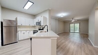 Located in Lewisville, TX, this single-story, 2-bedroom, 2-bathroom residence offers a well-designed open-concept layout that seamlessly connects the kitchen, dining, and living areas. The kitchen is a standout feature, equipped with white shaker cabinetry, a tile backsplash, stainless steel appliances including a refrigerator, electric range, and built-in microwave, along with a peninsula island featuring a white quartz countertop and undermount sink with a matte black faucet. Light wood-style flooring runs throughout the entire unit, creating a cohesive and modern aesthetic. The living room is accented with crown molding, a ceiling fan, and a sliding glass door that provides access to an outdoor balcony and fills the space with natural light. Both bedrooms are comfortably sized, each featuring a ceiling fan, large windows with blinds, and direct access to walk-in closets with built-in wire shelving. The bathrooms are finished with white vanity cabinetry, quartz countertops, matte black hardware, and a tub-shower combination. Additional highlights include a dedicated laundry area and two hallways connecting all areas of the unit efficiently. The overall palette of warm neutrals and bright white finishes lends the space a clean, contemporary feel.