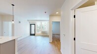 Located at 2463 Hogum Bay Rd NE in Lacey, WA, this well-appointed 2-bedroom, 2-bathroom unit offers a clean, modern aesthetic throughout its efficiently designed single-floor layout. Light wood-style flooring flows seamlessly across all living areas, lending warmth and continuity to the space.

The open-concept kitchen and living area serves as the heart of the unit. The kitchen is outfitted with taupe flat-front cabinetry, white quartz countertops, stainless steel appliances including a refrigerator and range, and a central island with a sink and pendant lighting above — ideal for both cooking and casual dining. Recessed lighting illuminates the kitchen and living area, which opens generously toward the entryway.

The primary bedroom is a comfortable, well-proportioned room featuring a closet with sliding doors and direct access to the hallway. A second bedroom provides a bright, versatile space with light-filled walls and the same consistent flooring. Both rooms offer a clean, neutral palette.

The two bathrooms are finished with light wood flooring, white fixtures, and modern hardware. One bathroom features a full tub-shower combo, while the other includes a vanity with dark drawer pulls. A private balcony accessible from the living area overlooks lush Pacific Northwest evergreen trees, bringing natural scenery into everyday living.
