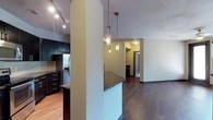 This single-floor residence showcases a cohesive contemporary design throughout its living spaces. The kitchen is a standout feature, outfitted with rich dark cabinetry, granite countertops, a white subway tile backsplash, and a full suite of stainless steel appliances including a French door refrigerator, electric range, built-in microwave, and dishwasher. A peninsula with a dark granite surface and pendant lighting overhead creates a natural divide between the kitchen and the adjoining living areas. Track lighting illuminates the kitchen, while hardwood-style flooring flows through the main living spaces, anchored by dark baseboards throughout.

The bedrooms offer plush carpeting underfoot, ceiling fans with light fixtures, and horizontal blinds on the windows. One bedroom features French doors, providing additional access and natural light. Ample closet space is present, with one room featuring a wide reach-in closet framed by dark panel doors with built-in shelving and hanging rods.

The bathroom is finished with a dual-sink vanity topped with dark granite, a large framed mirror, dark cabinetry below, and a tiled tub-shower combination, completing the unit's consistent, modern aesthetic.