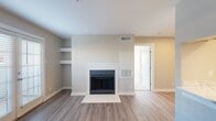 This well-appointed 1-bedroom, 1-bathroom residence offers a practical and comfortable single-floor layout with modern finishes throughout. The living room serves as the centerpiece of the home, featuring warm wood-look flooring, a white tile-surround fireplace, built-in wall shelving, and a set of French doors that invite natural light and provide outdoor access. The kitchen is efficiently designed with white shaker cabinetry, marble-style countertops, black appliances including a refrigerator, range, and dishwasher, and a pass-through counter window that opens to the living area — enhancing the sense of openness. A dedicated utility room with an electrical panel is accessible directly from the kitchen. The bedroom is carpeted for comfort, with two windows fitted with blinds that allow for ample natural light, a ceiling fan, and direct access to a walk-in closet with built-in shelving and hanging rods. The bathroom features a marble-style vanity countertop, white cabinetry, a large mirror, and a tiled shower. Neutral warm-gray tones and consistent finishes create a clean, cohesive aesthetic throughout the space.