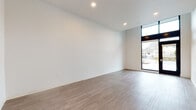 Located at 213 N Killingsworth Street in Portland, Oregon, this single-floor unit showcases a clean, modern aesthetic throughout. The open main living area features warm wood-look luxury vinyl flooring, crisp white walls, and recessed lighting that creates a bright and welcoming atmosphere. A striking floor-to-ceiling glass door and window panel floods the space with natural light and provides direct views to the exterior, lending the unit a contemporary, open feel.

The kitchen is efficiently designed with soft sage-green lower cabinetry paired with white upper cabinets, offering ample storage through a combination of drawers, doors, and open shelving. Light countertops provide a clean workspace, and the kitchen is equipped with a built-in cooktop, microwave, refrigerator, and a stainless steel sink — all thoughtfully arranged within a compact footprint. A hallway connects the main living area to the additional rooms, maintaining a logical and functional flow.

The additional rooms continue the same clean design language, with consistent flooring, white walls, and recessed lighting. The bathroom is finished with wood-look flooring, a walk-in shower with a grab bar for accessibility, and a toilet — all presented in a simple, utilitarian style. Overall, the space presents a cohesive, modern design that is bright, functional, and move-in ready.