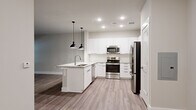 This single-floor residence presents a clean, contemporary design highlighted by wood-look plank flooring that flows seamlessly throughout the space. The open-concept layout connects the kitchen and living areas, creating a cohesive and functional environment.

The kitchen serves as a centerpiece, featuring crisp white shaker-style cabinetry extending to the ceiling for generous storage. A peninsula island with a granite-look countertop and undermount sink provides additional workspace and casual seating potential. A suite of stainless steel appliances — including a refrigerator, range, built-in microwave, and dishwasher — complement the modern aesthetic. Two matte black pendant lights hang above the island, adding a stylish contrast to the bright, recessed-lit space.

The living area is generously proportioned and bathed in natural light from a glass-panel door and adjacent window, offering access to the outdoors. Neutral gray walls provide a versatile backdrop throughout the unit.

The bathroom is well-appointed with a granite-topped vanity, undermount sink, framed mirror, and a tub-shower combination featuring subway tile surround and brushed nickel fixtures, completing the polished, move-in-ready interior.