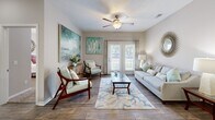 Located in Gulf Shores, Alabama, this well-appointed 2-bedroom, 2-bathroom residence offers a thoughtfully designed single-level layout. Wood-look flooring flows throughout the main living areas, lending a clean, cohesive aesthetic. The living room is bright and welcoming, featuring a ceiling fan, a coastal-inspired décor palette, and French doors that open to bring in natural light and outdoor views. Adjacent to the living room, the dining area accommodates a full table setting beneath a pendant light fixture. The kitchen is equipped with white shaker-style cabinetry, granite-look countertops, black appliances, a tile backsplash, and a peninsula with a sink — providing ample prep and storage space. A dedicated laundry room with a full-size washer and dryer adds everyday convenience. The primary bedroom is generously sized with plush carpeting, a ceiling fan, and a walk-in closet outfitted with wire shelving. The second bedroom also features carpet and a ceiling fan. Both bathrooms are finished with wood-look tile flooring, white vanities with granite-look countertops, and shower/tub combinations. The neutral color palette and coastal accents throughout create a calm, comfortable ambiance well-suited to the Gulf Shores setting.