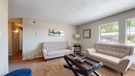 This single-floor residence offers a thoughtfully designed layout with distinct living, dining, kitchen, bedroom, and bathroom spaces, each finished with warm, neutral tones throughout. The living room features plush carpeting, textured ceilings, and a window that brings in natural light, creating a comfortable and inviting atmosphere. Adjacent to the living area, the dining room is accented by a ceiling fan with lighting, built-in shelving, and bold wall art that adds character to the space. The kitchen is a functional highlight, featuring grey cabinetry, light wood-style flooring, stainless steel appliances including a range, refrigerator, and dishwasher, as well as light countertops and a tile backsplash. Track lighting overhead ensures the space is well-lit. The bedrooms are carpeted and generously sized, each offering closet storage—including one room with a spacious walk-in closet fitted with dual hanging rods and center shelving. The bathroom is efficiently designed with wood-style flooring, a light blue vanity with a framed mirror, overhead lighting, and a shower-tub combination with a decorative curtain. Throughout the residence, the consistent use of neutral walls, carpet, and natural materials creates a cohesive, livable environment.