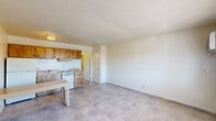 Located at 1106 W Bell Rd in Phoenix, AZ, this single-floor unit offers an efficient and functional layout across its compact footprint. The combined kitchen and living area forms the heart of the space, finished with neutral tile flooring throughout that contributes to a clean, cohesive look. The kitchen is equipped with warm-toned wood cabinetry — both upper and lower — along with a white electric range, refrigerator, a single-basin sink, and a yellow-toned countertop that extends to a built-in breakfast bar or table surface, providing a practical dining option. A range hood is mounted above the stove, and ample upper cabinet storage keeps the kitchen organized. The living area is open and bright, featuring a wall-mounted air conditioning unit and a window that allows natural light in while offering a view of the surrounding neighborhood. A textured popcorn ceiling is present throughout the unit. The two bathrooms include tile flooring consistent with the rest of the unit; one bathroom features a wood vanity with a yellow countertop, a mirror, and an adjoining room with a tiled tub and shower combination. A closet provides additional storage. The overall layout is straightforward and practical, suited for efficient everyday living.