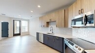 Located at 2902 N Arthur Ashe Blvd in Richmond, Virginia, this thoughtfully designed one-bedroom, one-bathroom unit offers a modern aesthetic with high-quality finishes throughout. The open kitchen is a standout feature, showcasing two-tone cabinetry with warm wood upper cabinets and dark charcoal lower cabinets accented by gold hardware. A classic white subway tile backsplash complements the clean quartz countertops, while a full suite of stainless steel appliances — including a refrigerator, range, microwave, and dishwasher — provides a fully equipped cooking space. Light hardwood flooring runs throughout the main living areas, enhancing the bright, airy atmosphere created by recessed lighting and natural light from windows. The bedroom offers a comfortable and well-proportioned retreat, finished with plush carpeting, a ceiling fan, and a window that brings in natural light. A dedicated closet provides convenient storage. The bathroom continues the unit's refined design language with dark cabinetry, gold-accented hardware, a white vanity top, and light wood flooring. Charcoal-toned interior doors with matte black hardware create a cohesive, contemporary look that ties the entire space together.
