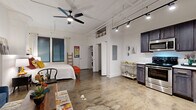 Located at 701 E Second St N in downtown Wichita, Kansas, this urban loft blends industrial character with modern comfort in an efficient, single-floor layout. The open-concept main area features striking polished concrete floors, soaring ceilings with exposed structural elements, and track lighting that illuminates the entire space. A large ceiling fan adds both style and function overhead.

The sleeping area is seamlessly integrated into the open floor plan, offering a cozy yet airy feel. The kitchen is a standout feature, outfitted with rich dark cabinetry, light stone countertops, and a full suite of stainless steel appliances including a range, microwave, dishwasher, and refrigerator. In-unit stacked washer and dryer units are conveniently tucked into a dedicated alcove.

The bathroom provides a clean, functional design with a glass-enclosed walk-in shower. Natural light filters through horizontal-slatted window blinds, enhancing the bright, white walls throughout. The industrial aesthetic is softened by warm furnishings and thoughtful design touches, creating an inviting urban retreat ideally situated in the heart of Wichita.