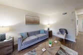 This two-floor residence offers a well-organized layout spread across two levels, connected by a carpeted staircase with a white handrail. The main level features a welcoming entryway with a large window that fills the space with natural light, alongside a coat rack and open shelving for practical storage. The living room is a comfortable, well-lit area with wood-style flooring, a large picture window overlooking the exterior, and a textured ceiling. Adjacent to the living room is a dedicated dining area with wood flooring and a wall-mounted mirror that adds depth to the space. The galley-style kitchen is equipped with white cabinetry, light speckled countertops, a double stainless steel sink, and a white range, with a window providing natural light and outdoor views. The upper level hosts two bedrooms, both carpeted for comfort. One bedroom features vaulted ceiling angles and a reach-in closet, while the primary bedroom includes an en-suite bathroom that also houses an in-unit washer. The bathroom features wood-style flooring, a vanity with a light countertop, and a towel rack. Throughout the space, neutral wall tones and consistent finishes create a cohesive and functional living environment.