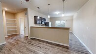 This single-floor, 1-bedroom, 1-bathroom residence offers a practical and comfortable layout across a compact yet efficiently designed footprint. The open-concept kitchen and living area serves as the heart of the home, featuring wood-look laminate flooring, neutral beige walls, and ceiling fans that enhance airflow and comfort. The kitchen is equipped with a full suite of stainless steel appliances — including a refrigerator, electric range, and over-the-range microwave — complemented by dark espresso cabinetry and light countertops. A raised breakfast bar peninsula with pendant lighting separates the kitchen from the living area, creating a natural and functional divide. Built-in open shelving adds convenient storage to the living space. The bedroom offers plush carpeting, a ceiling fan, a large window that admits natural light, and a dedicated closet with double doors for ample storage. The full bathroom includes a single-sink vanity with dark cabinetry, a light countertop, and wood-look flooring consistent with the rest of the home. Additional utility is provided by a dedicated laundry room and utility room, rounding out a thoughtfully organized layout well-suited for efficient everyday living.