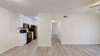 This single-story, one-bedroom, one-bathroom unit offers a functional and comfortable layout across a compact yet efficiently designed floor plan. The open-concept living and kitchen area forms the heart of the unit, where light wood-look vinyl flooring flows throughout, creating a cohesive and clean aesthetic. A ceiling fan with integrated lighting illuminates the living room, which benefits from natural light provided by a large sliding glass door fitted with vertical blinds and offering views of the surrounding greenery outside.

The galley-style kitchen is well-equipped, featuring white cabinetry on both sides, light stone-look countertops, a stainless steel sink, and a full suite of black appliances including a refrigerator, range, microwave, and dishwasher. The layout maximizes counter and storage space within the compact footprint.

The bedroom is carpeted for comfort and includes a ceiling fan, a closet, and a window for natural light. The room is generously sized relative to the overall floor plan, offering a peaceful retreat.

The bathroom is finished with wood-look tile flooring, a single-sink vanity with a speckled countertop, and a full bathtub with shower. Neutral warm tones and a textured ceiling are consistent throughout the unit, contributing to its clean and move-in ready appearance.