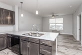 This single-floor unit offers a well-designed open-concept layout where the kitchen flows seamlessly into the living area. The kitchen is a standout feature, equipped with rich dark espresso cabinetry extending to the upper walls, light marble-style countertops, and black appliances including a refrigerator, range, and over-the-range microwave. A peninsula with a double stainless steel sink serves as a functional divider between the kitchen and living space, illuminated by stylish pendant lighting overhead. Light wood-style plank flooring runs throughout the main living areas, adding warmth and continuity.

The living area benefits from natural light through blinds-fitted windows and is equipped with a ceiling fan. Additional rooms feature the same ceiling fan fixtures, with some rooms finished in plush carpet and others in wood-style flooring. Each room includes windows with exterior views and individual climate control units, providing flexibility and comfort.

The bathroom is clean and functional, featuring a dark vanity with a marble-style countertop, a single sink, a combined tub and shower with a curtain rod, and neutral tile flooring. Throughout the unit, neutral gray walls and white trim create a cohesive, modern aesthetic suitable for a variety of furnishing styles.