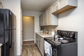 This single-floor residence offers a practical and comfortable layout across several well-defined living spaces. The galley-style kitchen is equipped with gray shaker-style upper and lower cabinets, light granite-look countertops, wood-look plank flooring, and black appliances including a four-burner electric range and full-size refrigerator. A passthrough connects the kitchen to the rest of the unit seamlessly.

The living area is generously sized, featuring neutral carpet, a ceiling fan, and a sliding glass door that opens to a private balcony, allowing for natural light and outdoor views. Baseboard heating runs throughout the carpeted bedrooms, each of which features windows overlooking mature trees. One bedroom includes a large open closet, while others benefit from multiple windows that bring in ample daylight.

The bathroom is finished with wood-look flooring, a white vanity with storage, a mirrored medicine cabinet, and a tub-shower combination. Neutral warm-gray walls are consistent throughout the unit, creating a cohesive and understated aesthetic. The 3D floor plan reveals an efficient, interconnected layout that maximizes the available living space across all rooms.