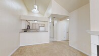 This single-floor residence is defined by its dramatic vaulted ceilings, which lend a sense of openness and volume throughout the main living areas. The open-concept layout connects the living room to the kitchen via a peninsula-style breakfast bar, making it an ideal space for everyday living and entertaining. The living room is anchored by a fireplace and features plush wall-to-wall carpeting, a ceiling fan, and tall windows that invite generous natural light. A pendant light fixture adds a functional focal point above the main living space.

The kitchen is efficiently laid out with light wood cabinetry, laminate countertops, tile flooring, and a full suite of appliances including a black electric range, over-the-range microwave, dishwasher, and refrigerator. A stainless steel sink completes the workspace.

The bedrooms continue the warm, carpeted aesthetic and are equipped with ceiling fans and windows with blinds. The primary bedroom stands out with notably high vaulted ceilings, dual windows for added light, and a closet with bifold doors. An additional bedroom offers a comfortable, well-proportioned layout.

Two bathrooms serve the home: one features a walk-in corner glass shower, a vanity with granite-style countertops, and a window for ventilation, while the second includes a combined tub and shower with tile flooring. Both bathrooms are finished in neutral, clean tones throughout.