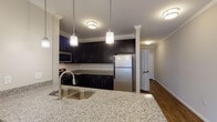 Located at 6411 Farmgate Rd in Raleigh, NC, this single-floor residence offers a well-appointed layout with thoughtful finishes throughout. The kitchen is a standout feature, showcasing granite countertops, dark espresso cabinetry, a classic subway tile backsplash, and a full suite of stainless steel appliances including a refrigerator, gas range, and built-in microwave. Pendant lighting and a deep undermount sink add both style and function to the space. Rich hardwood-style flooring extends through the kitchen and main living areas, complemented by elegant crown molding and neutral warm-toned walls that create a cohesive, polished atmosphere. The open living and dining area is accented by a chandelier and benefits from an open sightline into the kitchen, making the space feel connected and expansive. The bedroom features plush carpeting, a ceiling fan, and a window that brings in natural light with views of the surrounding neighborhood. The bathroom is finished with tile flooring, a soaking tub with subway tile surround, and clean, neutral tones. Throughout the unit, white panel doors, crown molding, and consistent finishes lend a refined, move-in-ready character to this comfortable Raleigh residence.