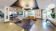 Located at 120 Border St in East Boston's waterfront neighborhood, this thoughtfully designed community lounge delivers a rich, nautical-inspired aesthetic across a single expansive floor. Polished concrete floors run throughout, lending an industrial edge that contrasts beautifully with warm, curated furnishings and layered textures.

The entry area sets the tone immediately, featuring a striking ship-rigging mural that spans the wall alongside bold sliding barn-style doors, hinting at the maritime character woven throughout the space. A reception-style counter and seating near the entrance offer a welcoming transition into the interior.

The main lounge area is anchored by a large sectional sofa in deep navy, surrounded by leather accent chairs and layered rugs beneath a dramatic circular pendant light fixture. Teal wainscoting and an ornate patterned ceiling insert add depth and personality, while curated wall art, decorative oars, and rope-wrapped pendant lights reinforce the coastal theme.

A communal dining area features a long wooden table with navy upholstered chairs, lit by nautical globe pendants. Adjacent to this, a reclaimed wood feature wall frames a mounted flat-screen TV, flanked by additional lounge seating. Large windows throughout invite abundant natural light and views of the surrounding greenery, creating an open, airy ambiance that balances design richness with everyday comfort.