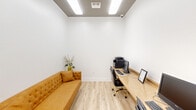 Located at 25455 Borough Park Dr in Spring, TX, this efficiently designed office space offers a polished and functional environment suited for professional use. The room is finished with crisp white walls, crown molding, and light-toned wood-look flooring that together create a clean, welcoming atmosphere. Overhead, recessed fluorescent lighting provides bright, even illumination throughout the space. A long, built-in granite-top workstation runs along one wall, accommodating a desktop computer, printer, and additional office equipment — making it well-equipped for administrative tasks. A stylish tufted caramel-colored sofa is positioned along the opposite wall, offering comfortable seating for clients or visitors. A gold-accented side table with a floral arrangement adds a refined decorative touch. The room also features a frosted-glass panel door that opens to an adjacent area, allowing for natural flow between spaces. A security camera is mounted near the ceiling, and an HVAC vent ensures climate control. The overall design strikes a balance between professional utility and inviting aesthetics, making this space well-suited for client-facing office functions or consultation purposes.