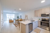 Located at 3640 Blue Fin Way in Fort Myers, Florida, this two-story residence showcases a clean, modern coastal aesthetic throughout. The open-concept main level is anchored by a well-designed kitchen featuring light wood cabinetry, gleaming white quartz countertops, stainless steel appliances, and a spacious island with bar seating — ideal for both everyday living and entertaining. Large-format tile flooring runs through the main living areas, while the living room offers a welcoming, airy atmosphere with a staircase leading to the upper level. The dining area is accented by a decorative macramé wall piece, adding a touch of artisan charm. Upstairs, the bedrooms are finished with warm hardwood flooring and benefit from generous natural light through wide windows dressed with clean white blinds. Ceiling fans provide comfort throughout. The bedrooms are complemented by spacious walk-in closets with full wire shelving systems. The bathroom features floor-to-ceiling neutral tile work and a frameless sliding glass shower enclosure with dual showerheads, lending a refined, spa-like quality. The overall palette of soft whites, warm woods, and coastal-inspired accents creates a serene and cohesive atmosphere throughout the home.