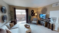 This single-floor residence offers a well-organized layout with a variety of functional living spaces. The living room serves as the heart of the home, featuring plush wall-to-wall carpeting, a textured ceiling, and a sliding glass door that opens to a private balcony — allowing natural light to flow in and providing an outdoor seating area. The entry area connects seamlessly to the living space, which is accented by warm, neutral-toned walls.

The galley-style kitchen is efficiently designed with warm oak cabinetry lining both sides, white appliances including a refrigerator and range, and light countertops with a stainless steel sink. Tile flooring runs throughout the kitchen, offering a practical and clean finish.

The bedroom is a comfortable retreat, complete with soft carpeting, a ceiling fan with integrated lighting, and a closet with bifold doors. Natural light enters through a window dressed with curtains, and textured ceilings carry throughout the room.

The bathroom features a wide vanity with oak cabinetry and a large mirror illuminated by a row of overhead lights. A separate bathtub and shower enclosure finished in white tile provides a clean, classic look. Overall, the space presents a cozy and practical living environment with consistent finishes throughout.