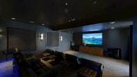 Located at 950 E 3rd St in the Arts District of Los Angeles, this private screening room delivers a true cinematic experience in a thoughtfully designed, self-contained space. The room is finished in deep, dark tones throughout — from the dark-painted ceiling to the charcoal and slate-blue walls — creating an immersive, distraction-free environment ideal for film viewing.

The seating arrangement features multiple rows of plush black leather reclining chairs and sofas, tiered on a raised platform toward the rear to ensure unobstructed sightlines for all viewers. Low-profile accent tables accompany the seating, while vibrant blue LED strip lighting beneath the raised tier adds a dramatic, theater-like atmosphere.

At the front of the room, a large projection screen dominates the wall, paired with a substantial media console in warm wood tones that houses the AV equipment. Ceiling-mounted in-ceiling speakers and recessed lighting provide both acoustic performance and controlled illumination. Elegant vertical wall sconces offer soft, ambient light along the side walls, complemented by acoustic panel treatments that enhance sound quality.

A popcorn machine adds a classic cinematic touch, and the room is accessed through a heavy soundproofed door framed by a dramatic red curtain, reinforcing the private theater aesthetic. This space offers a complete, high-end screening experience in the heart of Los Angeles.