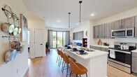 This single-floor, one-bedroom, one-bathroom unit offers a thoughtfully designed open-concept layout that maximizes its compact footprint. The kitchen and living area flow seamlessly together, anchored by a sleek white quartz island with an undermount double sink, pendant lighting, and seating for multiple bar stools — ideal for casual dining or entertaining. The kitchen features gray shaker-style cabinetry extending to the ceiling, stainless steel appliances including a French-door refrigerator, electric range, built-in microwave, and dishwasher, all set against light hardwood-style flooring that runs throughout the main living area.

The living room benefits from large sliding glass doors that open to a private balcony, allowing generous natural light and outdoor views. The bedroom offers carpeted flooring, a large window with outdoor views, and notable ceiling height, creating a comfortable and airy retreat. Multiple closet doors provide ample storage within the bedroom.

The bathroom features a clean, minimalist design with light-toned walls and hardwood-style flooring consistent with the rest of the unit. Throughout, the unit maintains a contemporary aesthetic with crisp white walls, recessed lighting, and black hardware accents that tie the design together cohesively.