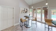 Located at 3400 Sweetwater Rd in Lawrenceville, Georgia, this single-floor community clubhouse offers a well-appointed gathering space designed for both relaxation and socializing. The facility is divided into two distinct areas, each with its own character and function.

The sunlit gathering room is a standout feature, boasting soaring vaulted ceilings with elegant crown molding and large floor-to-ceiling windows that flood the space with natural light. Neutral tile flooring runs throughout, and multiple high-top round tables with modern bar seating provide a casual, social atmosphere. French doors open directly to the outdoor pool area, offering seamless indoor-outdoor connectivity and scenic views of the lush, landscaped surroundings and brick-accented pool deck. Pendant lighting adds a contemporary touch overhead.

The adjacent lounge area features warm hardwood-style flooring, a textured ceiling, and recessed lighting. Comfortable seating — including a sofa and accent chairs — is arranged around a mid-century style coffee table, creating an inviting space for unwinding. A wall-mounted flat-screen television serves as a focal point, while decorative elements such as framed artwork and floral arrangements contribute to the welcoming ambiance. An arched doorway connects the spaces, reinforcing the cohesive and thoughtfully designed layout throughout the clubhouse.