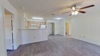 This single-floor, 2-bedroom, 1-bathroom home offers a functional and well-organized layout designed for comfortable everyday living. The open-concept kitchen and living room form the heart of the space, with the kitchen featuring light wood cabinetry, white appliances including a refrigerator and range, an under-cabinet range hood, and a peninsula with a light stone-style countertop that provides additional prep space and separates the kitchen from the living area. A large pantry closet with louvered doors offers generous storage directly off the kitchen. Hardwood-style laminate flooring flows consistently throughout the entire home, complemented by neutral white walls that create a bright, clean aesthetic. Ceiling fans with integrated lighting fixtures are present in the living room and primary bedroom, contributing to both air circulation and ambient lighting. The spacious primary bedroom includes a reach-in closet with louvered doors and a window that allows natural light. The second bedroom also features a closet and a window with blinds. The shared bathroom is equipped with a tiled tub-shower combination and standard fixtures. A dedicated laundry area and two closets round out the practical amenities of this efficiently designed home.