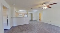 This single-floor, 2-bedroom, 1-bathroom home offers a functional and well-organized layout designed for comfortable everyday living. The open-concept kitchen and living room form the heart of the space, with the kitchen featuring light wood cabinetry, white appliances including a refrigerator and range, an under-cabinet range hood, and a peninsula with a light stone-style countertop that provides additional prep space and separates the kitchen from the living area. A large pantry closet with louvered doors offers generous storage directly off the kitchen. Hardwood-style laminate flooring flows consistently throughout the entire home, complemented by neutral white walls that create a bright, clean aesthetic. Ceiling fans with integrated lighting fixtures are present in the living room and primary bedroom, contributing to both air circulation and ambient lighting. The spacious primary bedroom includes a reach-in closet with louvered doors and a window that allows natural light. The second bedroom also features a closet and a window with blinds. The shared bathroom is equipped with a tiled tub-shower combination and standard fixtures. A dedicated laundry area and two closets round out the practical amenities of this efficiently designed home.