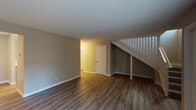 Located at 18540 SW Boones Ferry Rd in Tualatin, Oregon, this two-story residence offers a clean, updated interior with a cohesive neutral palette throughout. The main level features an open living area with wood-look vinyl plank flooring, textured ceilings, and a ceiling fan. A staircase with white balusters connects to the upper level, and additional doors provide access to utility or storage spaces tucked beneath the stairs. The kitchen is well-appointed with light gray cabinetry, white quartz countertops, a deep stainless steel undermount sink with a brushed gold faucet, a window overlooking the greenery outside, and white appliances including a range and dishwasher. Upper cabinetry offers ample storage. The bedrooms are bright and generously sized, each featuring wood-look flooring, large windows with slatted blinds that invite natural light, and baseboard heating. One bedroom includes a sliding-door closet with built-in shelving and hanging space. The bathroom is finished with a white quartz vanity, brushed gold fixtures, a large wall mirror with contemporary lighting, and a full tub and shower combination. The overall ambiance is fresh, functional, and move-in ready.