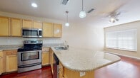Located at 909 Apollo Beach Blvd in Apollo Beach, Florida, this single-floor residence offers a well-designed layout with a cohesive blend of practical finishes and comfortable living spaces. The open-concept living and kitchen area is anchored by rich, warm hardwood flooring that extends throughout the main living space, creating an inviting atmosphere. A ceiling fan overhead provides comfort, while recessed lighting and pendant lights above the kitchen island add both function and style. The kitchen is well-appointed with light maple cabinetry, granite countertops, a curved breakfast bar island, and a full suite of stainless steel appliances including a refrigerator, range, microwave, and dishwasher. A stacked washer and dryer unit is conveniently integrated adjacent to the kitchen. The bedrooms are carpeted for comfort and feature neutral tones, with windows that allow natural light to filter in. One bedroom includes a closet with bi-fold doors and built-in shelving. The bathroom is finished with tile flooring, a granite-topped vanity with maple cabinetry, and a tiled tub-shower combination. The overall ambiance is clean, functional, and well-maintained, making this a practical and comfortable home in the Apollo Beach community.